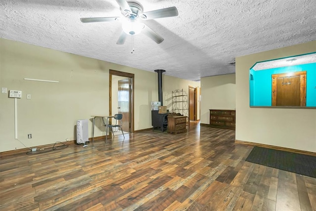 interior space featuring a wood stove, ceiling fan, dark wood-type flooring, and a textured ceiling