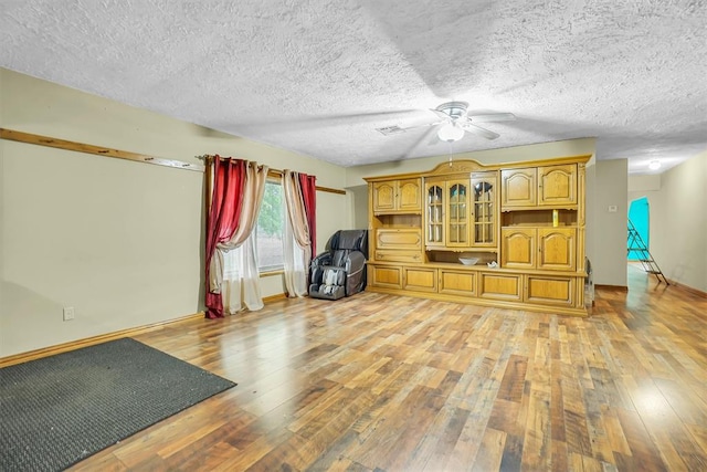 workout area featuring ceiling fan, light wood-type flooring, and a textured ceiling