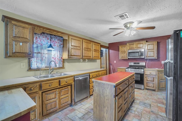 kitchen with a center island, sink, ceiling fan, a textured ceiling, and stainless steel appliances