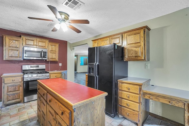 kitchen featuring a textured ceiling, ceiling fan, a center island, and stainless steel appliances