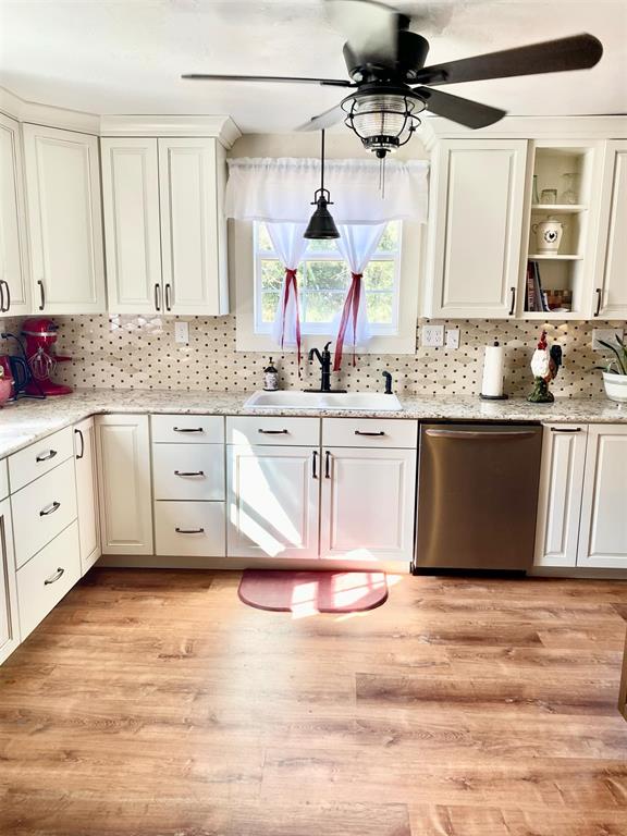 kitchen with dishwasher, light stone countertops, light wood-type flooring, and sink