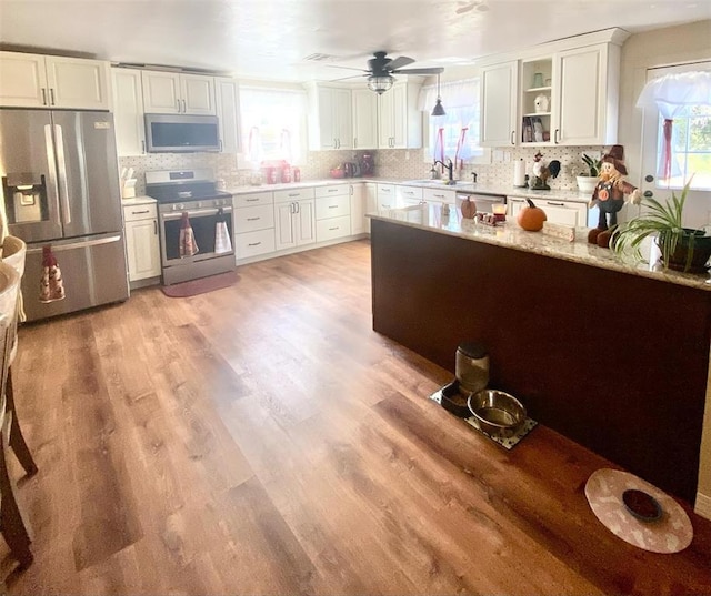 kitchen with light stone countertops, tasteful backsplash, light hardwood / wood-style flooring, white cabinets, and appliances with stainless steel finishes