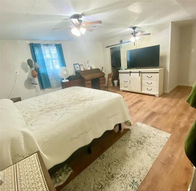 bedroom featuring a barn door, light hardwood / wood-style floors, and ceiling fan