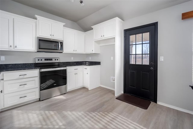 kitchen featuring white cabinetry, lofted ceiling, dark stone countertops, light hardwood / wood-style floors, and stainless steel appliances