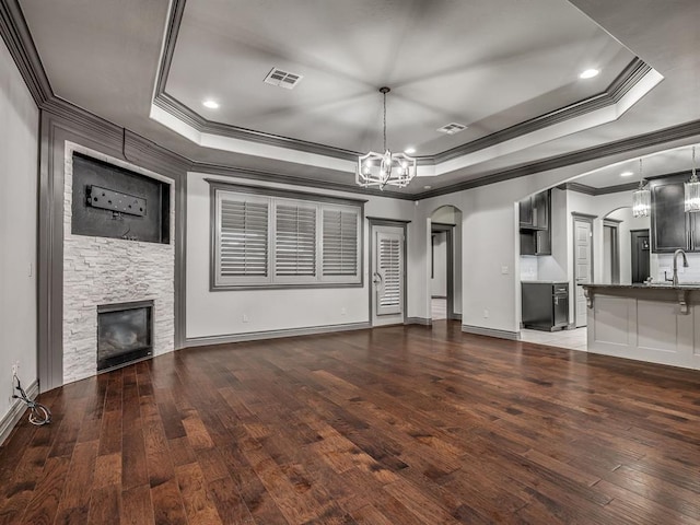 unfurnished living room with a raised ceiling, dark wood-type flooring, and crown molding