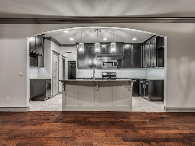 kitchen with appliances with stainless steel finishes, sink, pendant lighting, a center island with sink, and light hardwood / wood-style floors