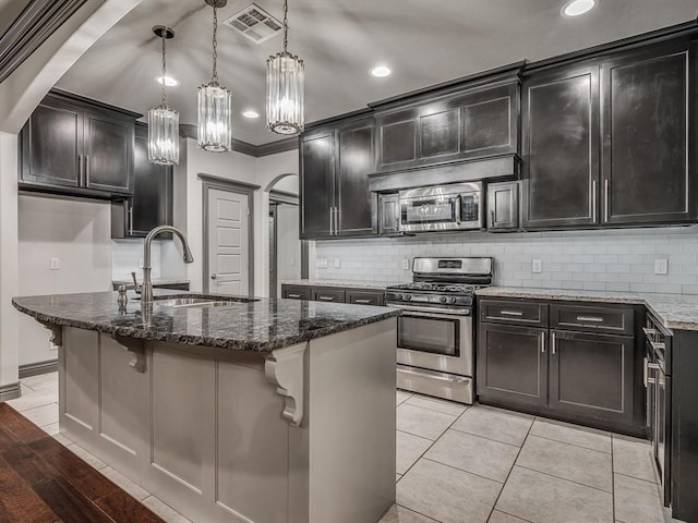 kitchen featuring hanging light fixtures, a center island with sink, dark stone counters, and appliances with stainless steel finishes