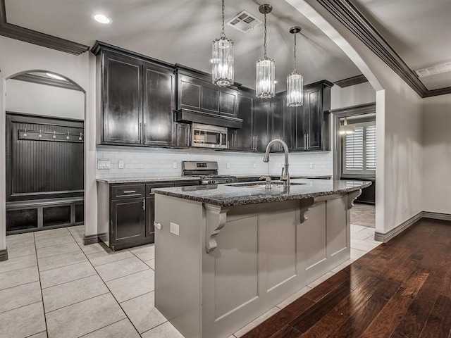 kitchen with light wood-type flooring, stainless steel appliances, sink, pendant lighting, and an island with sink