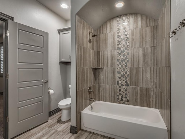 bathroom featuring wood-type flooring, toilet, and tiled shower / bath