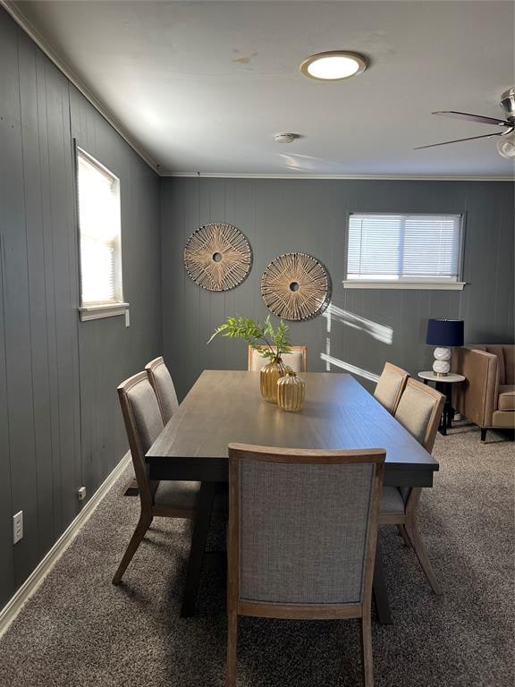 carpeted dining space featuring ceiling fan, ornamental molding, and wooden walls