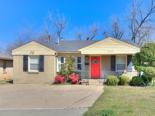 view of front of property with brick siding, covered porch, a front lawn, and roof with shingles