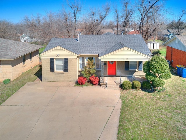 bungalow-style house featuring a front lawn, covered porch, concrete driveway, roof with shingles, and brick siding