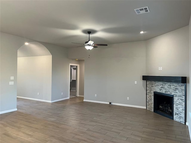 unfurnished living room with ceiling fan and a stone fireplace