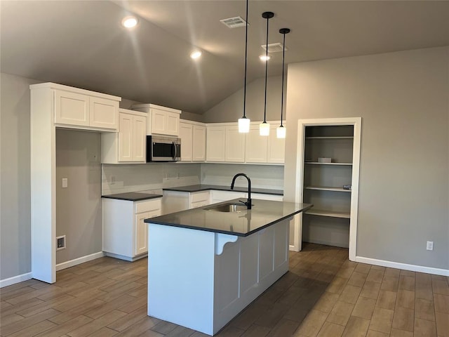 kitchen with sink, white cabinets, vaulted ceiling, hanging light fixtures, and a kitchen island with sink