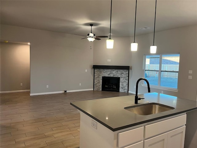 kitchen with a center island with sink, white cabinets, ceiling fan, a fireplace, and sink