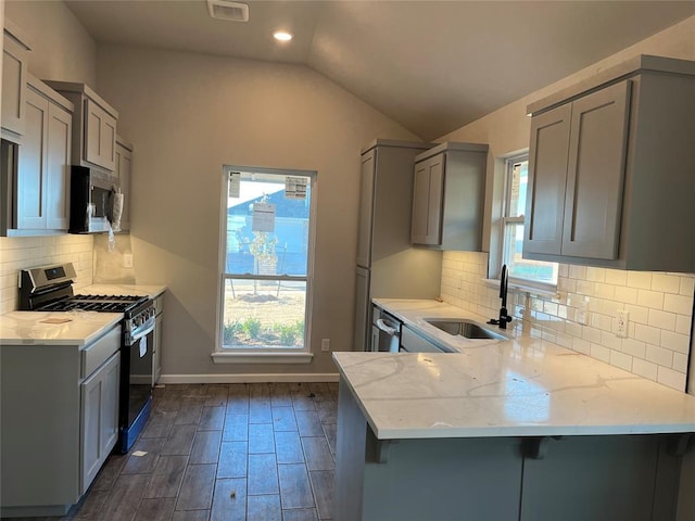 kitchen featuring vaulted ceiling, gray cabinets, appliances with stainless steel finishes, a kitchen bar, and kitchen peninsula