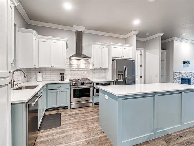 kitchen featuring sink, stainless steel appliances, wall chimney range hood, light hardwood / wood-style floors, and white cabinets