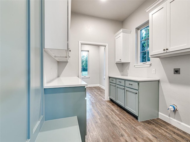 clothes washing area featuring hookup for an electric dryer, hardwood / wood-style flooring, a wealth of natural light, and cabinets