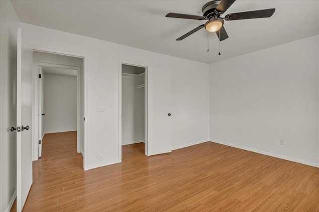 unfurnished bedroom featuring ceiling fan, a walk in closet, light wood-type flooring, and a closet