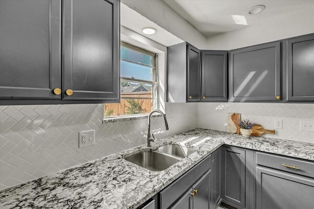 kitchen featuring light stone countertops, backsplash, gray cabinetry, and sink