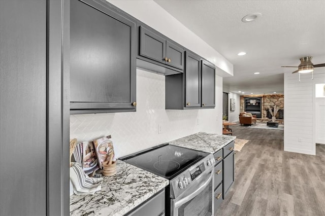 kitchen featuring light stone counters, ceiling fan, light hardwood / wood-style floors, a stone fireplace, and stainless steel range with electric cooktop