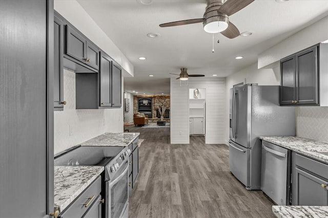 kitchen featuring ceiling fan, light stone counters, wood-type flooring, and appliances with stainless steel finishes