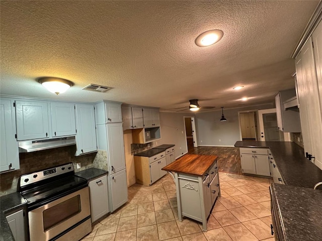 kitchen featuring a textured ceiling, butcher block counters, light tile patterned flooring, and stainless steel range with electric stovetop