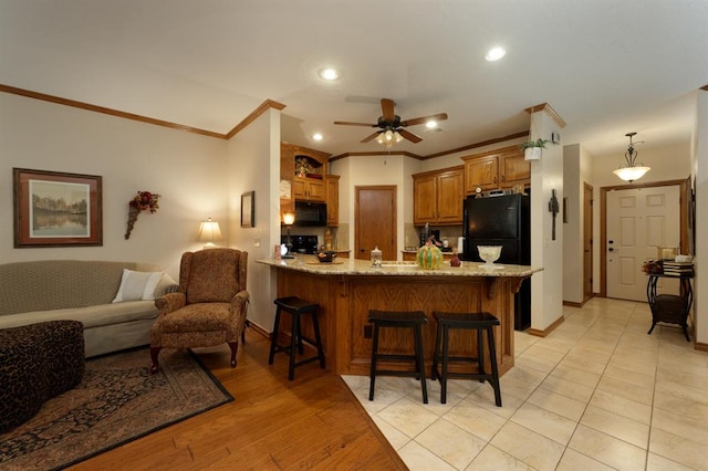 kitchen featuring black appliances, crown molding, kitchen peninsula, and a breakfast bar area