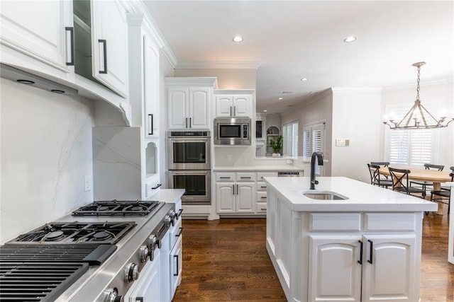 kitchen featuring a kitchen island with sink, an inviting chandelier, sink, appliances with stainless steel finishes, and white cabinetry