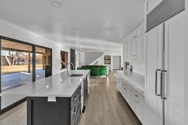 kitchen with light hardwood / wood-style floors, white cabinetry, a kitchen island with sink, and sink