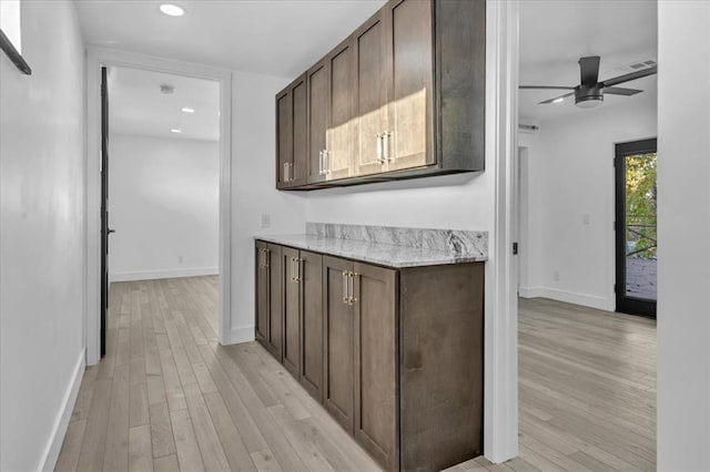 interior space with dark brown cabinetry, light stone countertops, light hardwood / wood-style flooring, and ceiling fan