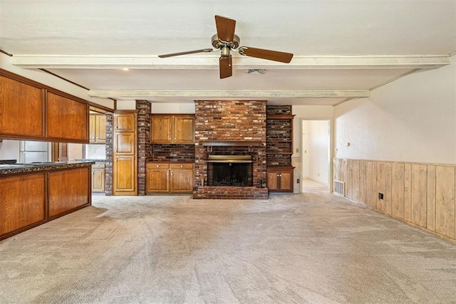 unfurnished living room with beam ceiling, ceiling fan, wooden walls, light carpet, and a fireplace