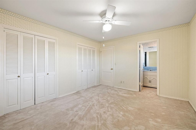 unfurnished bedroom with two closets, connected bathroom, light colored carpet, and ceiling fan