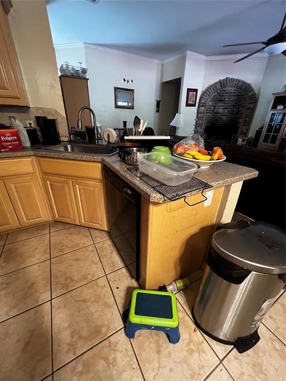 kitchen with sink, a brick fireplace, ornamental molding, black dishwasher, and kitchen peninsula