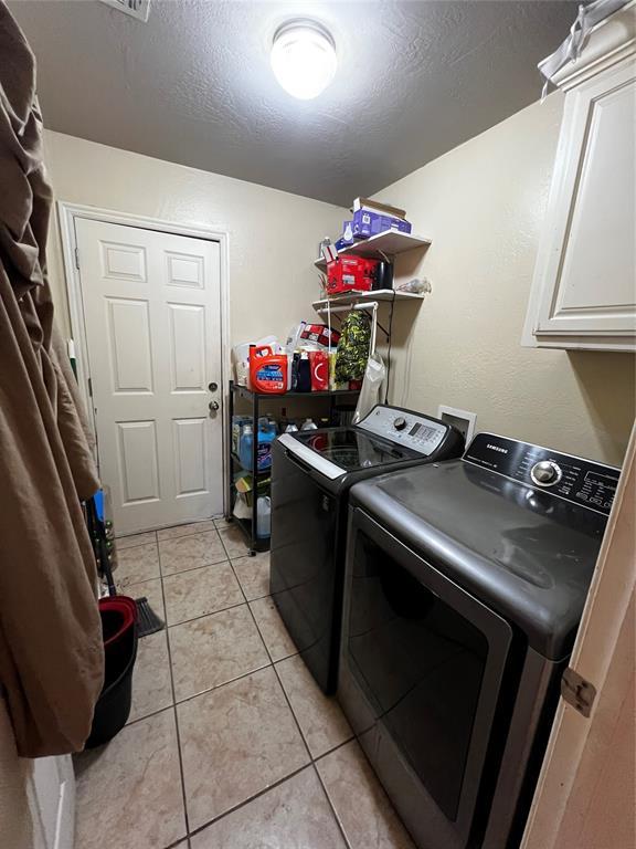 washroom featuring cabinets, light tile patterned floors, washing machine and dryer, and a textured ceiling