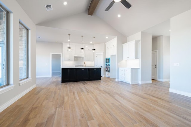 kitchen with white cabinetry, beamed ceiling, pendant lighting, and a large island with sink