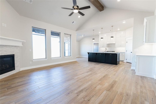 unfurnished living room featuring beamed ceiling, a fireplace, sink, light hardwood / wood-style flooring, and ceiling fan