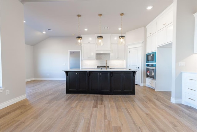 kitchen with decorative light fixtures, stainless steel oven, a kitchen island with sink, and light hardwood / wood-style floors