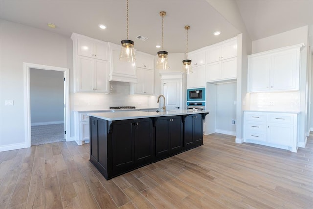 kitchen featuring black appliances, light wood-type flooring, white cabinetry, and a center island with sink