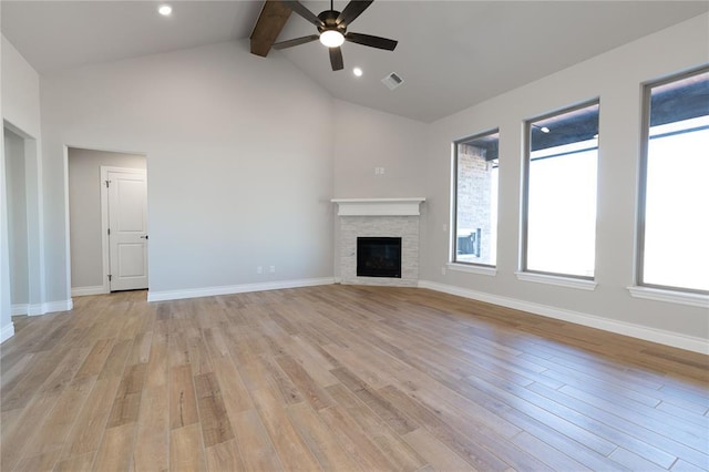 unfurnished living room with ceiling fan, a stone fireplace, vaulted ceiling with beams, and light hardwood / wood-style floors