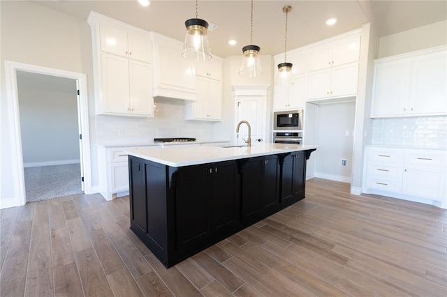 kitchen with light countertops, white cabinetry, built in microwave, stainless steel oven, and a sink