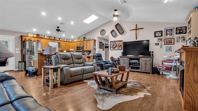 living room with vaulted ceiling with skylight, ceiling fan, and light hardwood / wood-style flooring