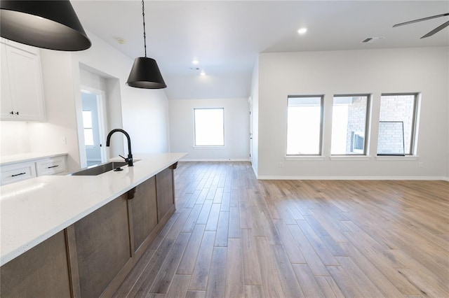 kitchen with white cabinets, sink, hanging light fixtures, ceiling fan, and light hardwood / wood-style floors