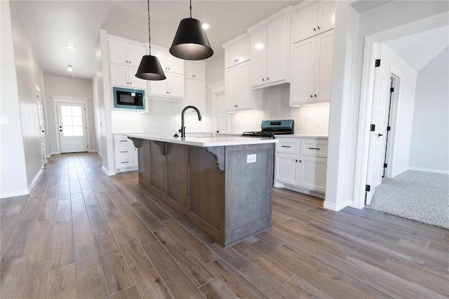 kitchen with white cabinetry, black microwave, stainless steel electric stove, and an island with sink