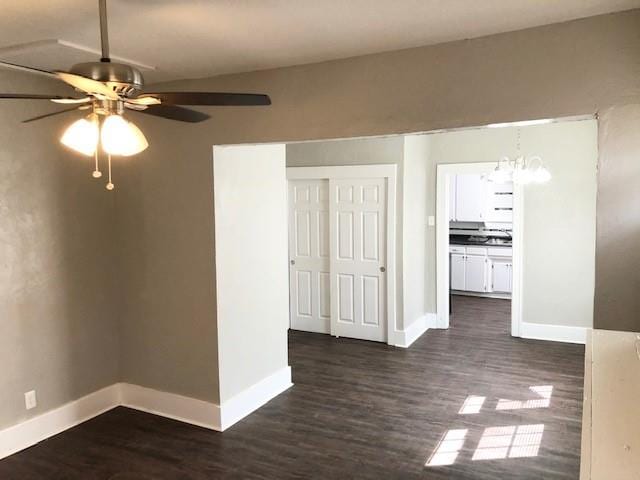 empty room with ceiling fan with notable chandelier and dark hardwood / wood-style flooring