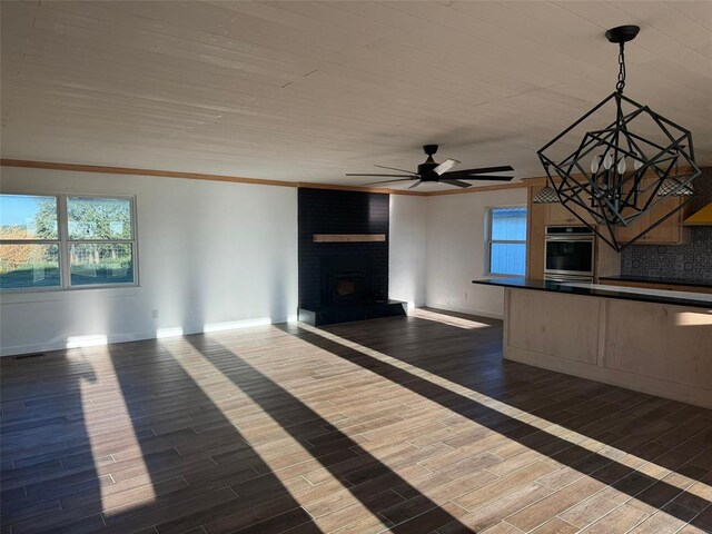 unfurnished living room featuring a fireplace, ornamental molding, ceiling fan, and dark wood-type flooring