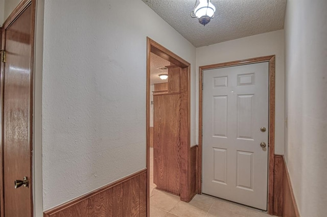 entryway featuring wood walls, light tile patterned floors, and a textured ceiling