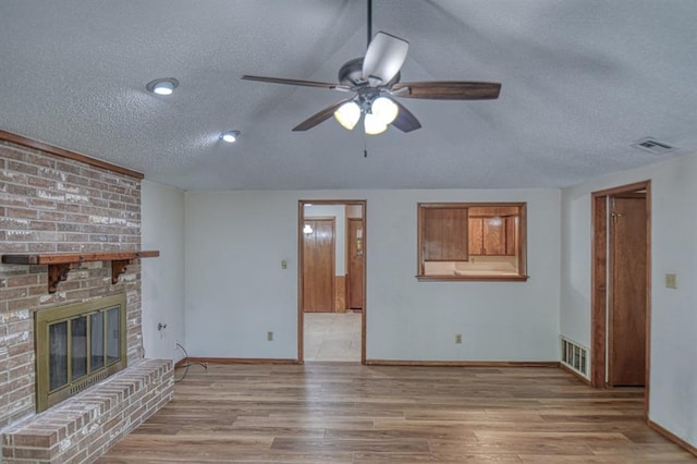 unfurnished living room featuring a fireplace, a textured ceiling, light hardwood / wood-style flooring, and ceiling fan