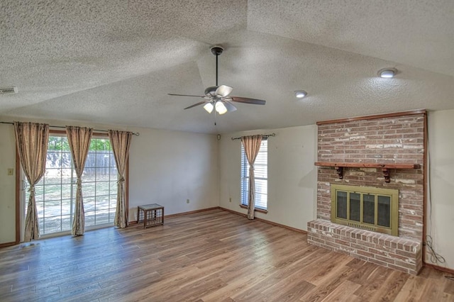 unfurnished living room with wood-type flooring, a textured ceiling, a brick fireplace, and ceiling fan