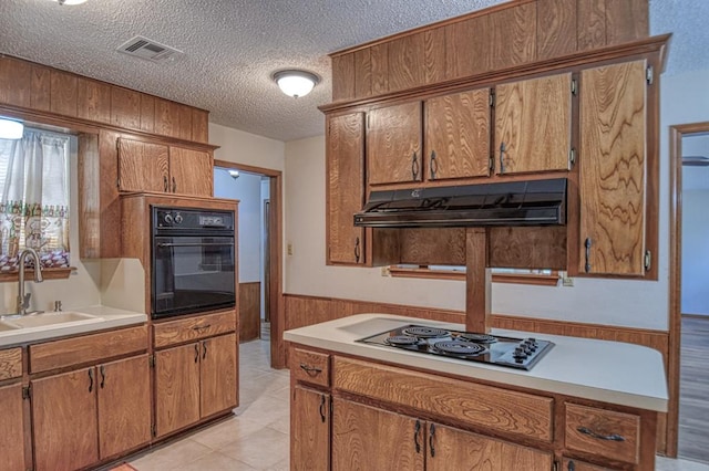 kitchen featuring a textured ceiling, wooden walls, sink, oven, and stainless steel gas stovetop